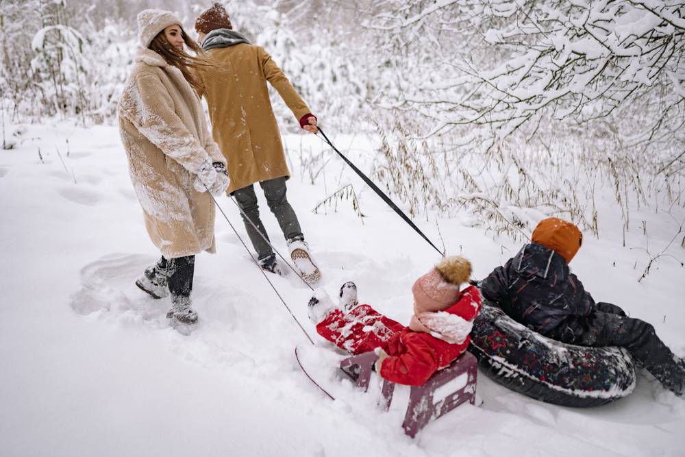 Parents pulling two kids on sleds through fresh snow