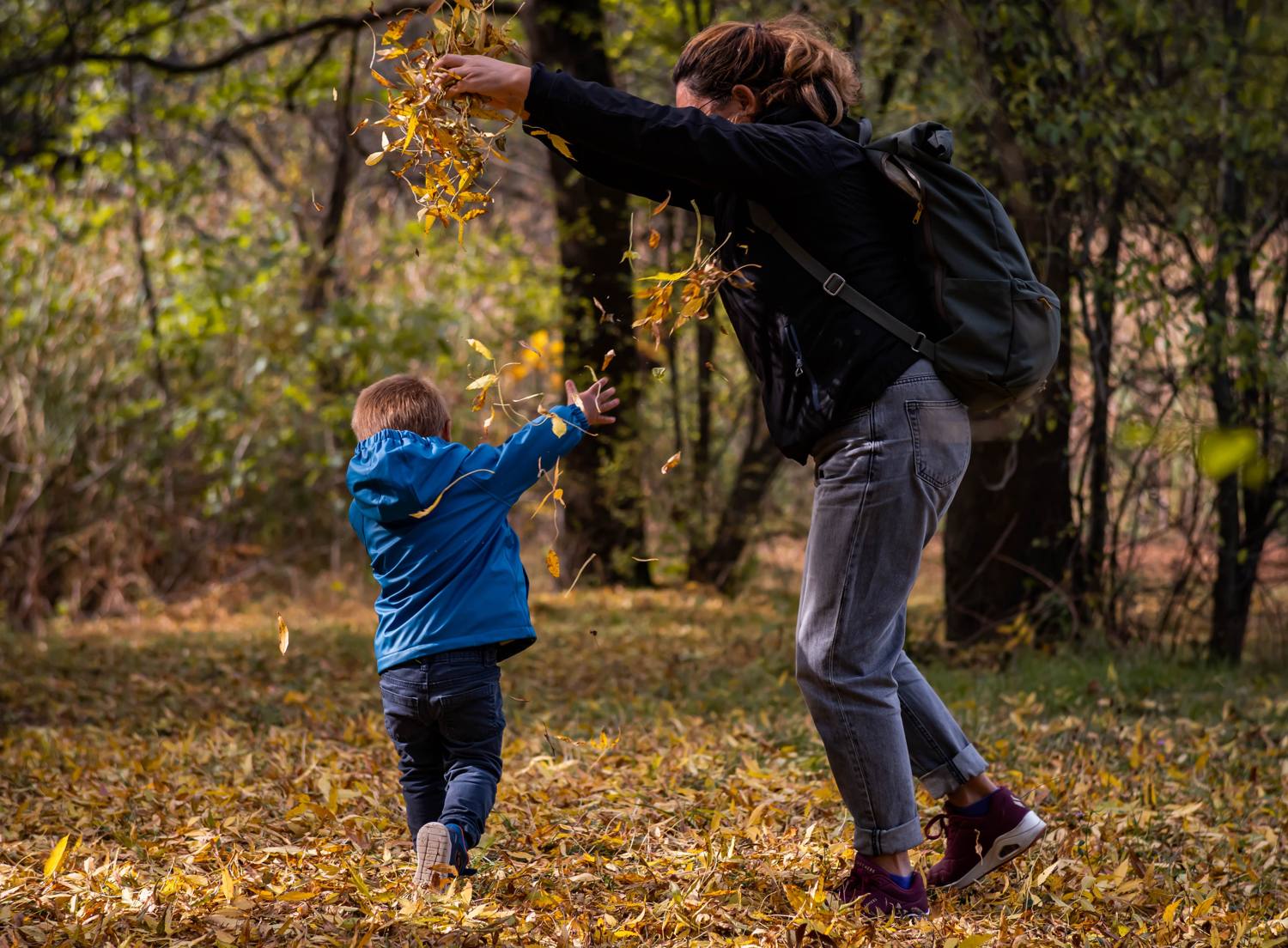 A mom tossing autumn leaves over her laughing little boy