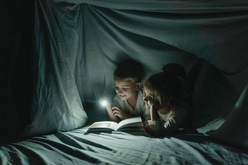 Kids reading under a blanket by flashlight